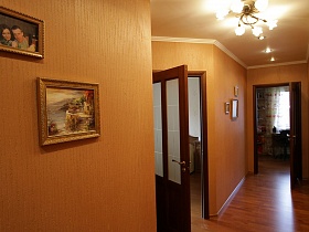 цветочная люстра на белом потолке коридора с картинами и фотографиями на светло-коричневых стенах современной трехкомнатной квартиры с детской комнатой