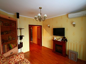 обогреватель, коричневый электрокамин, телевизор и бра с белыми плафонами, люстра на белом потолке гостиной трехкомнатной квартиры с детской
