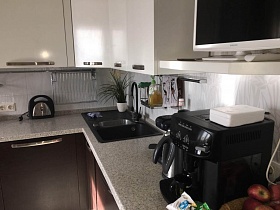 черная кофеварка, электрочайник, тостер и комнатный цветок на светлой столешнице темной мебельной стенки светлой кухни трехкомнатной квартиры с дизайнерским ремонтом