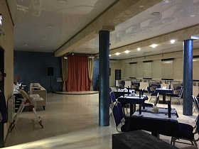 детские стульчики для кормления у стены, сцена с занавесом, уютные сервированные столы в просторном зале ресторана с натяжным потолком и жалюзи на окнах
