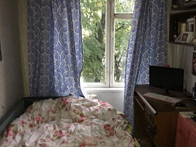 цветные голубые шторы с белыми разводами на окне спальни с нежно-розовым постельным на деревянной кровати двухкомнатной квартиры