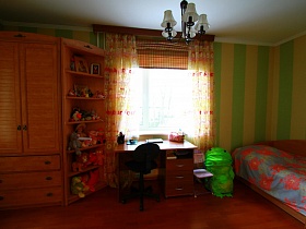 коричневый угловой шкаф с боковыми полками, письменный стол, деревянная кровать с цветным постельным у стены с полосатыми зелеными обоями в детской спальной комнате государственного служащего